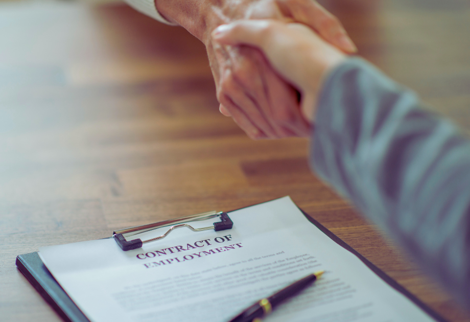 two people shaking hands over a table and an employment contract